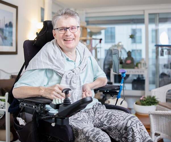 57-jähriger Mann, weiße Haare, Brille mit körperlicher Behinderung, sitzend in einem Rollstuhl