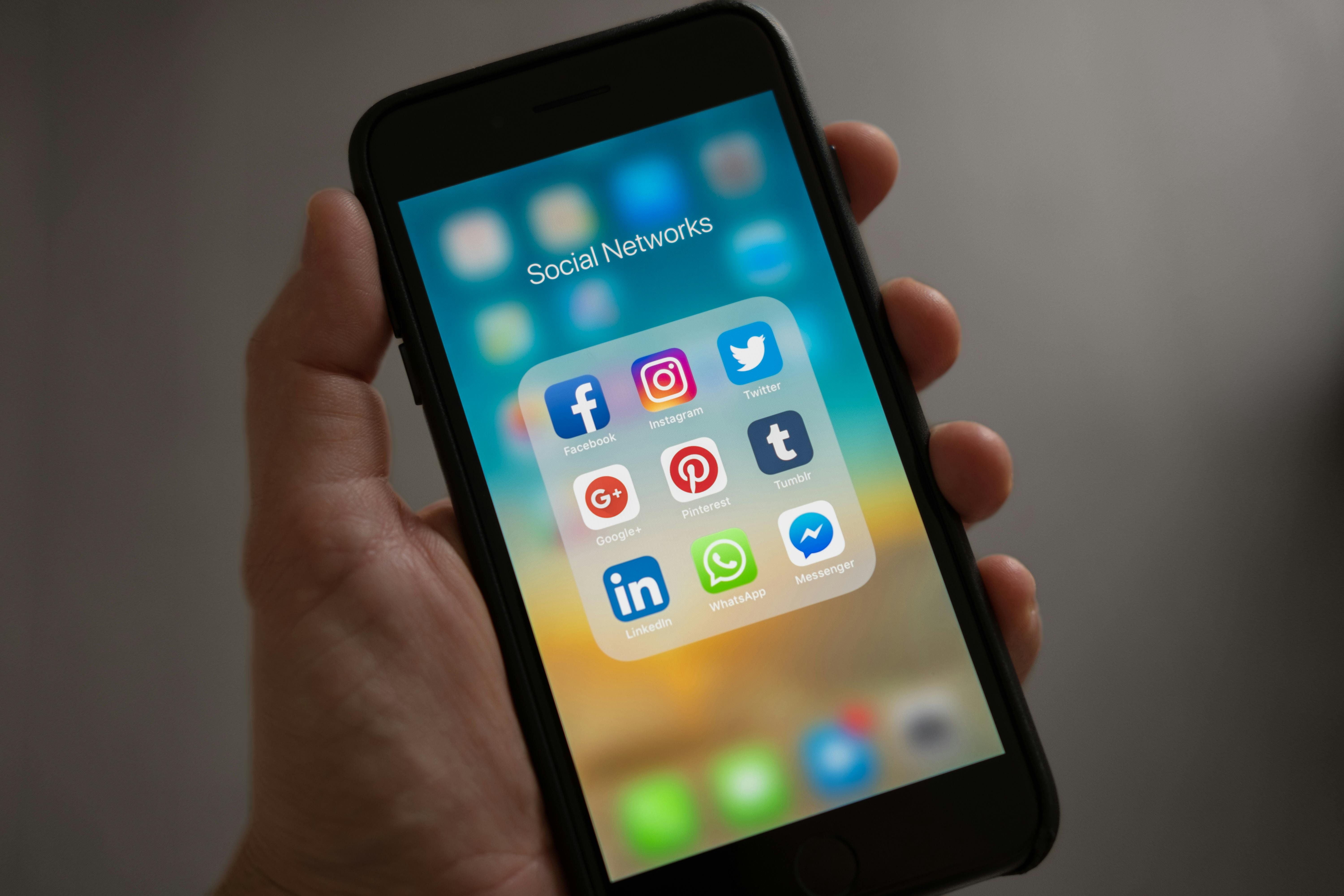 Eine Hand hält ein Smartphone. Auf dem Bildschirm des Smartphones sind verschiedene Social-Media-Apps in einem Ordner mit der Bezeichnung