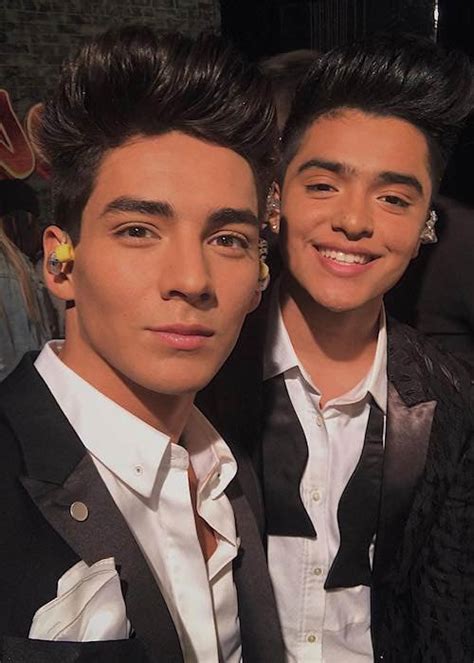 Zeigt Schauspieler Chance Perez mit einem Kollegen. Sie beide sehen sich ähnlich. Sie haben beide Earpieces im Ohr, als kommen sie gerade von der Bühne. Sie tragen beide einen schwarzen Anzug und haben dunkle Haare und Augen.