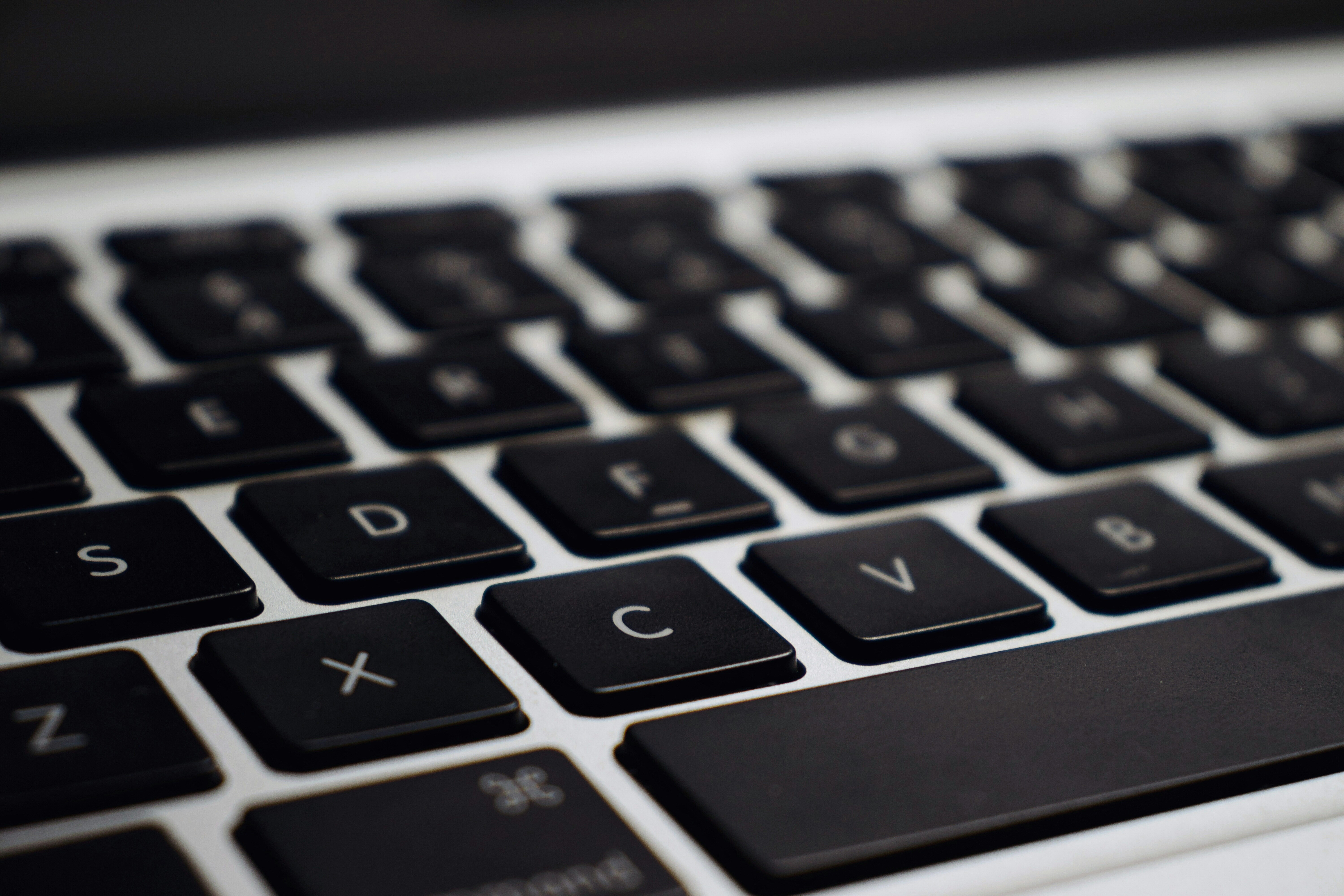 Eine Nahaufnahme einer Computertastatur. Die Tasten sind schwarz mit weißen Buchstaben. Man sieht die Buchstaben S, D, F, C, V, X und Z deutlich. Die Tasten sind in einem leicht schrägen Winkel fotografiert, was eine dreidimensionale Perspektive erzeugt. Die Oberfläche der Tastatur ist silberfarben.