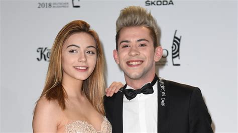 Daniel Negroni mit Freundin links neben ihm. Beide haben blondierte Haare und lächeln in die Kamera. Sie trägt ein schulterfreies crème-weisses Kleid, er einen dunklen Anzug mit weissem Hemd und schwarzer Kravatte.
