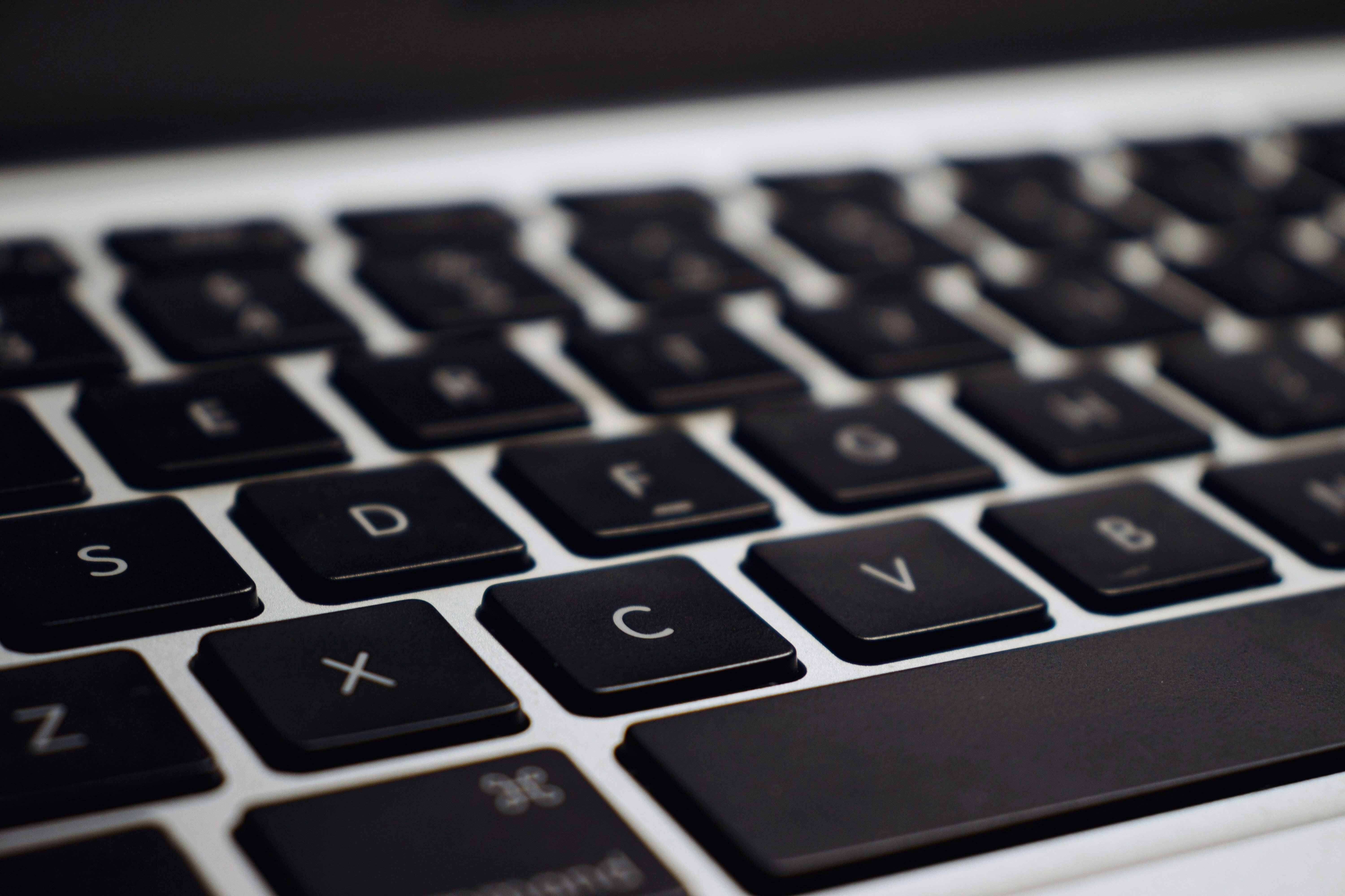 Eine Nahaufnahme einer Computertastatur. Die Tasten sind schwarz mit weißen Buchstaben. Man sieht die Buchstaben S, D, F, C, V, X und Z deutlich. Die Tasten sind in einem leicht schrägen Winkel fotografiert, was eine dreidimensionale Perspektive erzeugt. Die Oberfläche der Tastatur ist silberfarben.